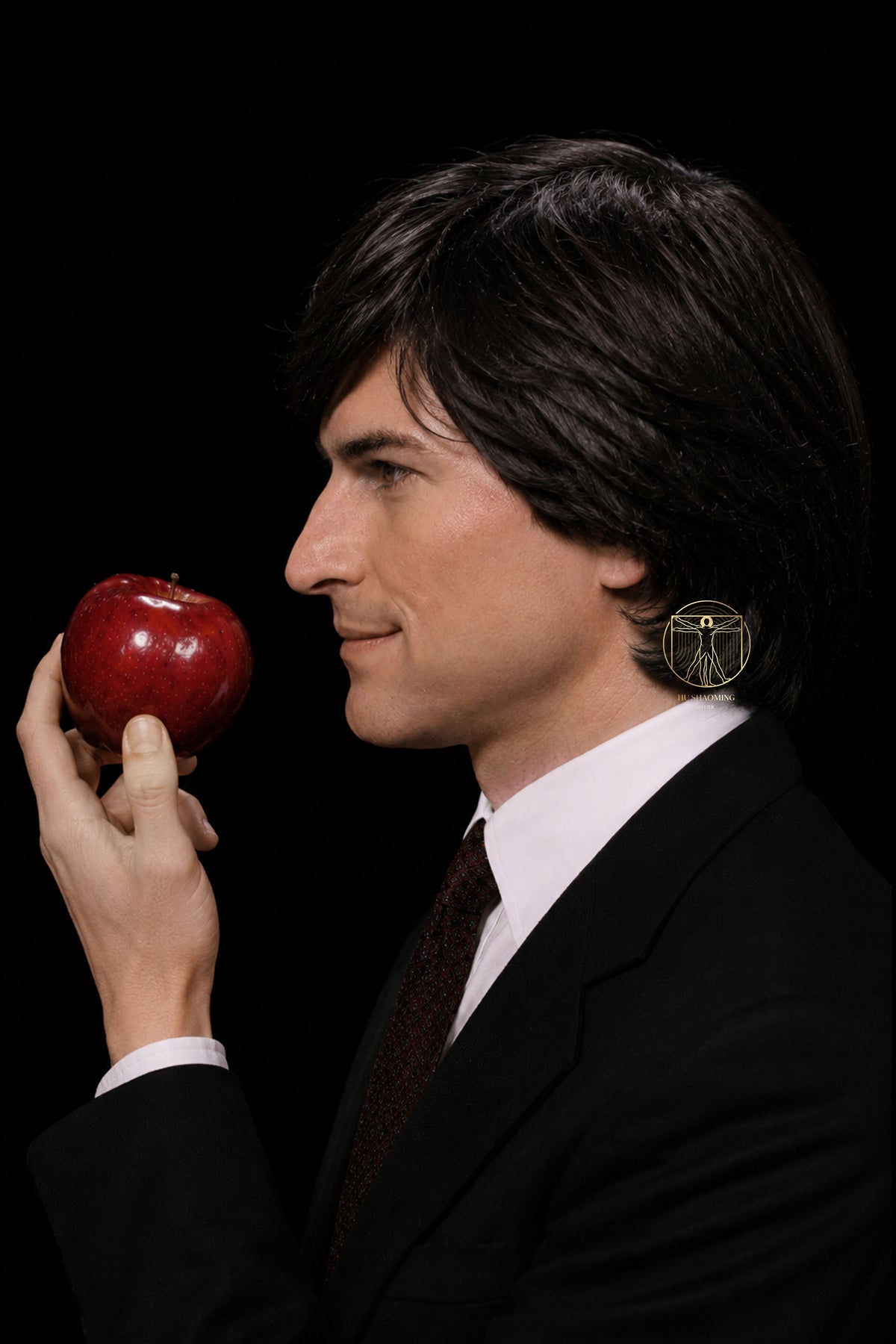 Side profile view of young Steve Jobs silicone bust looking at a red apple